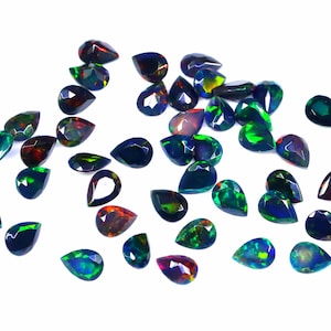 May include: A collection of pear-shaped black opals with iridescent green, blue, and red hues. The opals are scattered on a white background.