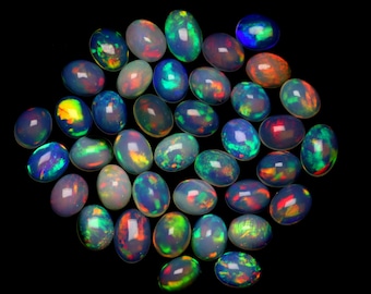 Puede incluir: Un conjunto de ópalos ovalados con un tono oscuro, que muestran un juego de colores. Los ópalos exhiben una gama de colores, incluyendo verde, azul, naranja y amarillo, sobre un fondo negro. Estas piedras preciosas están pulidas y lisas.