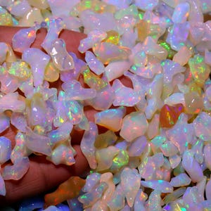 May include: A close-up of a pile of iridescent white opal chips. The chips are various shapes and sizes, with a rainbow of colors shimmering through them.