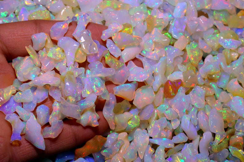 May include: A close-up of a pile of iridescent white opal chips. The chips are various shapes and sizes, with a rainbow of colors shimmering through them.