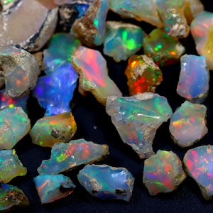 May include: A collection of rough opal gemstones in various shades of white, blue, green, and orange. The opals are iridescent and have a natural, raw appearance.