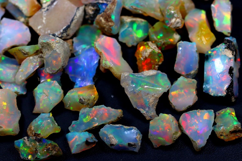 May include: A collection of rough opal gemstones in various shades of white, blue, green, and orange. The opals are iridescent and have a natural, raw appearance.