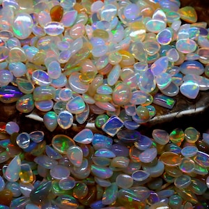 Op de afbeelding: Een verzameling opalen in verschillende vormen en maten, met een scala aan kleuren, waaronder wit, blauw, groen en oranje. De edelstenen hebben een parelmoerglans, die het licht reflecteert en een glinsterend effect cre&euml;ert. De opalen zijn verspreid.