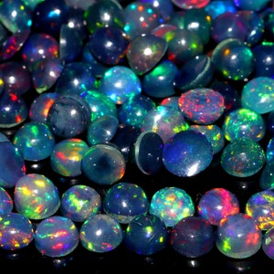 Può includere: Una collezione di cabochon di opale rotondi e iridescenti in varie tonalità di blu, verde e rosso. Gli opali sono lisci e lucidi, con un'alta lucentezza.