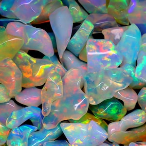 Könnte beinhalten: Eine Sammlung von regenbogenfarbenen Opal-Edelsteinen in verschiedenen Formen und Größen. Die Opale sind eine Mischung aus Weiß, Blau, Grün und Orange.