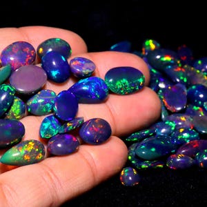 May include: A collection of oval-shaped black opals with iridescent rainbow colors. The opals are displayed on a hand.