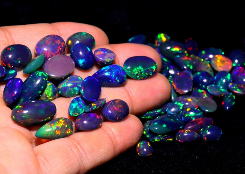 May include: A collection of oval-shaped black opals with iridescent rainbow colors. The opals are displayed on a hand.