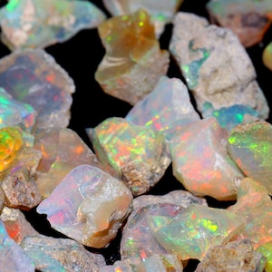 Peut inclure: Une collection de pierres précieuses d'opale brute dans différentes nuances de blanc, de vert et d'orange. Les opales sont irisées et ont une finition naturelle non polie.