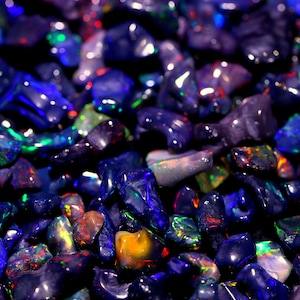 May include: A close-up view of a collection of loose, iridescent blue and purple opals. The opals are various shapes and sizes, and they shimmer and reflect light.