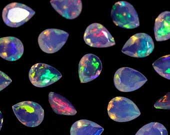 May include: A collection of pear-shaped opals with iridescent colors, including green, blue, and purple, on a black background.