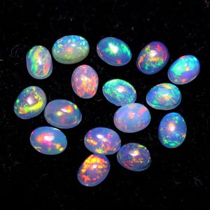 Puede incluir: Una colección de piedras preciosas de ópalo de forma ovalada en varios tonos de azul, verde y rosa. Los ópalos son iridiscentes y tienen una base blanca lechosa.