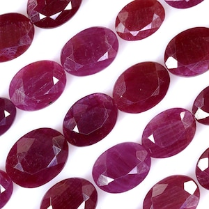May include: A strand of oval-shaped ruby beads with a faceted finish. The beads are a deep red colour and have a glossy sheen.