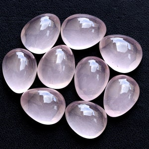 Puede incluir: Nueve piedras de cuarzo rosa lisas, de forma ovalada y de diferentes tamaños, dispuestas en círculo sobre una superficie negra.