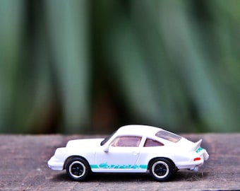 May include: White toy car with a green stripe and the word "Carrera" on the side. The car is sitting on a wooden surface.