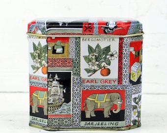 May include: A vintage tin box with a colorful design featuring elephants, ships, and floral patterns. The text on the box reads "Earl Grey", "Darjeeling", and "Bergamot", suggesting it is for tea storage.