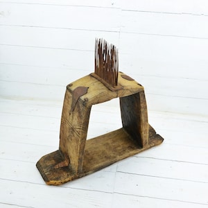 Peut inclure: Un outil en bois avec un cadre rectangulaire et une rangée de dents métalliques sur le dessus. Le cadre est en bois brut et a un aspect usé et rustique.