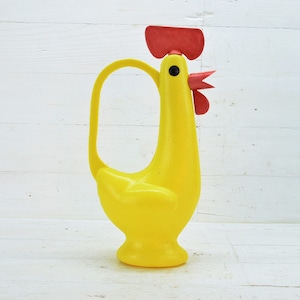 Könnte beinhalten: Gelbe Plastik-Gießkanne in Form eines Hahns mit rotem Kamm und Kehllappen. Die Gießkanne hat einen Griff und einen Ausguss.