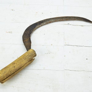 Op de afbeelding: Een vintage, roestige, metalen sikkel met een houten handvat. Het handvat is gebarsten en verweerd.