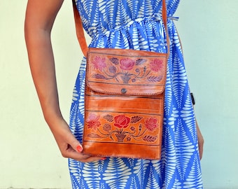 May include: A brown leather crossbody bag with floral embroidery in shades of red, orange, and green. The bag has a flap closure and a strap that can be adjusted.