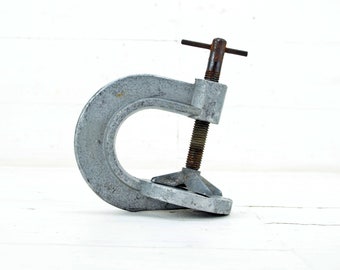May include: A silver metal C-clamp with a rusty screw and a T-shaped handle.