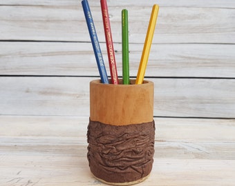 May include: A brown ceramic pencil holder with a textured, wood-like design. Four colored pencils are in the holder: blue, red, green, and yellow.