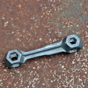 K&ouml;nnte beinhalten: Ein silberner Schraubenschl&uuml;ssel mit zwei sechseckigen &Ouml;ffnungen an jedem Ende. Der Schraubenschl&uuml;ssel liegt auf einer rostigen Metalloberfl&auml;che.