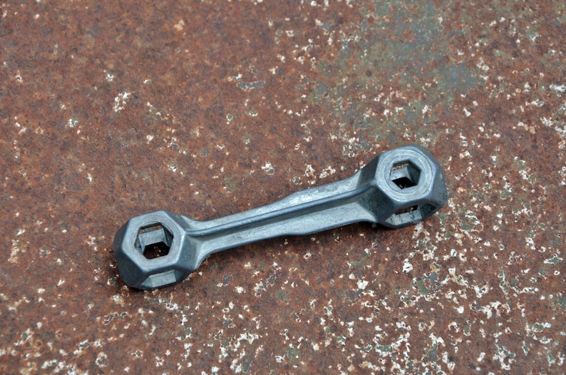K&ouml;nnte beinhalten: Ein silberner Schraubenschl&uuml;ssel mit zwei sechseckigen &Ouml;ffnungen an jedem Ende. Der Schraubenschl&uuml;ssel liegt auf einer rostigen Metalloberfl&auml;che.
