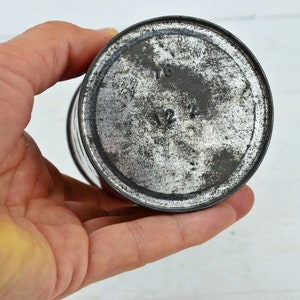 May include: Close-up of the bottom of a silver metal tin with the numbers 1/6 and 1/2 printed on the bottom.