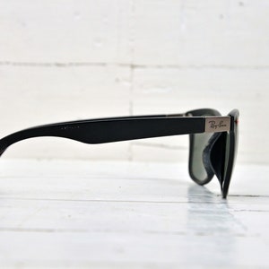 K&ouml;nnte beinhalten: Schwarze Sonnenbrille mit roten Akzenten an den B&uuml;geln und einem silbernen Ray-Ban-Logo an der Seite.