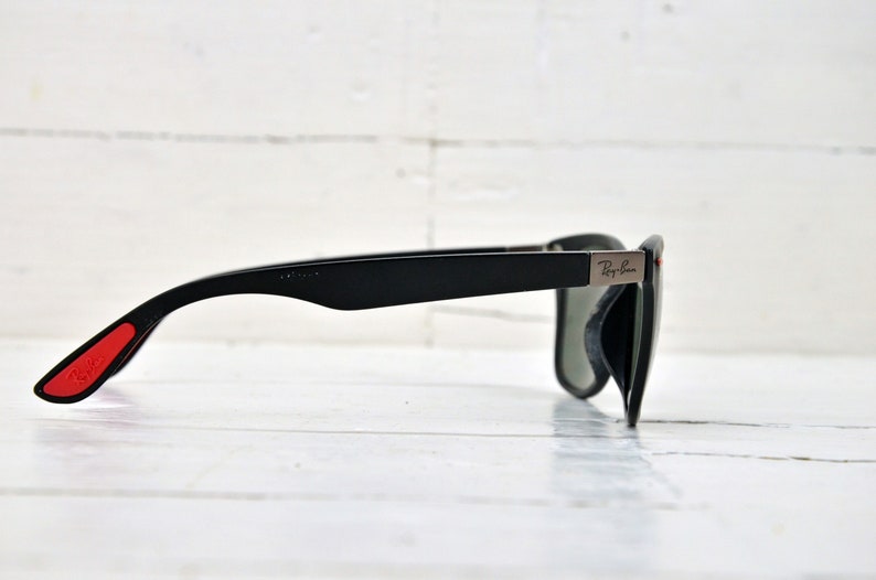K&ouml;nnte beinhalten: Schwarze Sonnenbrille mit roten Akzenten an den B&uuml;geln und einem silbernen Ray-Ban-Logo an der Seite.
