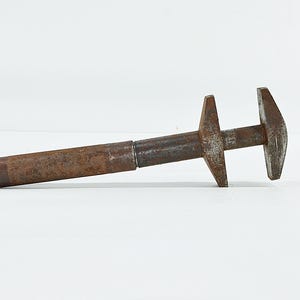 May include: A vintage, rusted metal adjustable wrench featuring a textured, cylindrical handle and a sliding jaw mechanism. The tool displays significant oxidation and wear across its entire surface, with a dark brown, weathered patina throughout.