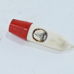 Puede incluir: Un silbato de recuerdo vintage con una boquilla roja texturizada y un cuerpo color crema. Un pequeño emblema circular con un edificio y la palabra "Leipzig" está incrustado en el cuerpo. El silbato tiene un pequeño agujero en el extremo.