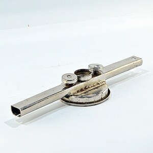 May include: A silver metal tool featuring a rectangular bar and three circular elements. The tool has a cylindrical base and two small, round caps. The design appears industrial and functional, set against a white backdrop.