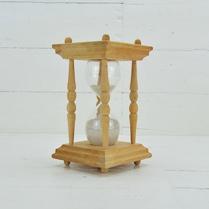 Peut inclure: Un sablier en bois avec un bulbe en verre transparent et un sablier à sable blanc. Le sablier est posé sur une surface en bois blanc.