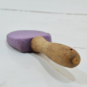 Puede incluir: Un bloque de lija morado con un mango de madera. El mango est&aacute; desgastado y tiene un agujero en el extremo.