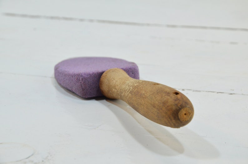 Puede incluir: Un bloque de lija morado con un mango de madera. El mango est&aacute; desgastado y tiene un agujero en el extremo.