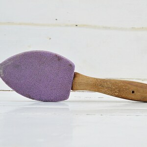 Puede incluir: Un abrillantador de zapatos de ante morado con un mango de madera. El mango tiene dos agujeros.
