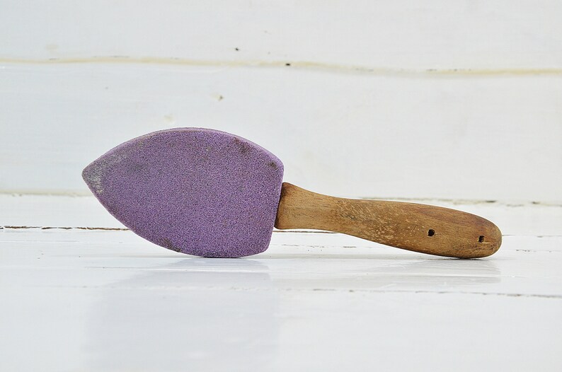 Puede incluir: Un abrillantador de zapatos de ante morado con un mango de madera. El mango tiene dos agujeros.