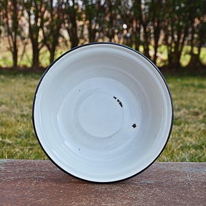 May include: White enamel bowl with a black rim. The bowl is slightly chipped on the inside.