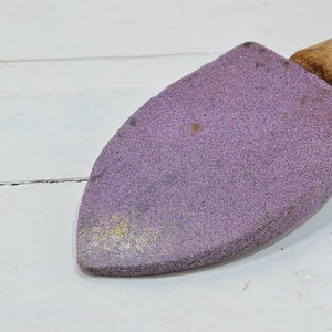Puede incluir: Una piedra de afilar de color p&uacute;rpura con un mango de madera. La piedra se utiliza para afilar cuchillos y otras herramientas.
