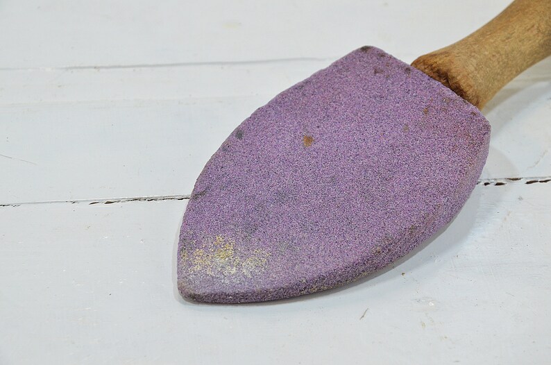 Puede incluir: Una piedra de afilar de color p&uacute;rpura con un mango de madera. La piedra se utiliza para afilar cuchillos y otras herramientas.