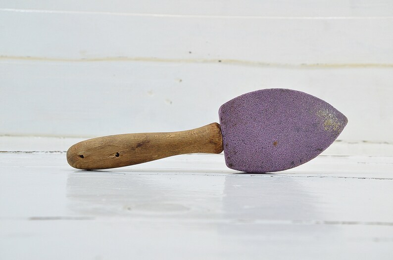 Puede incluir: Una plancha de hierro p&uacute;rpura con mango de madera y punta redondeada.