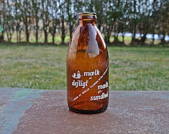 Puede incluir: Una botella de leche de vidrio marrón con texto blanco que dice "Mælk er dejligt" y "giv mælk sundhed".