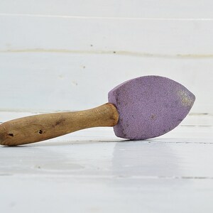 Puede incluir: Una piedra de afilar de color morado con mango de madera.