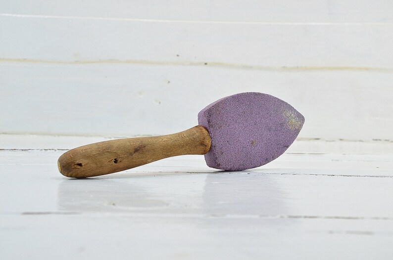 Puede incluir: Una piedra de afilar de color morado con mango de madera.