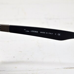 K&ouml;nnte beinhalten: Schwarze Sonnenbrille mit dunkelgrauen Gl&auml;sern und einem schwarzen Gestell. Das Gestell tr&auml;gt den Aufdruck "LITEFORCE MADE IN ITALY K CE" auf der Innenseite.