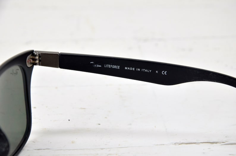 K&ouml;nnte beinhalten: Schwarze Sonnenbrille mit dunkelgrauen Gl&auml;sern und einem schwarzen Gestell. Das Gestell tr&auml;gt den Aufdruck "LITEFORCE MADE IN ITALY K CE" auf der Innenseite.