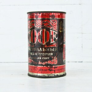 May include: A vintage red and black metal can with the word "KOФE" in gold lettering. The can is labeled "натуральный без цикория высший сорт" and has a faded, worn look.