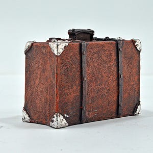 Könnte beinhalten: Ein brauner Vintage-Koffer mit Metallverzierungen und einer abgenutzten Lederoberfläche.