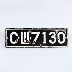May include: A rectangular black and white license plate with the text "CU 7130". The plate has a distressed, rusty appearance, with white lettering against a black background. The edges show signs of wear.